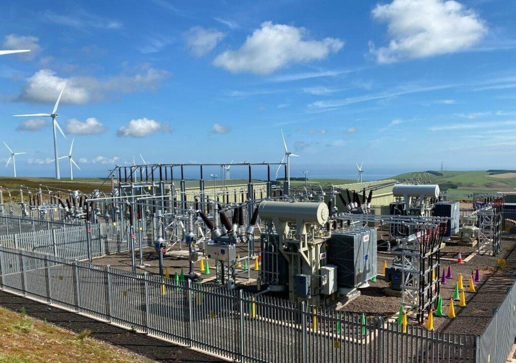 A modern solar farm or wind power plant featuring a Compact Sub-Station installed beside renewable energy generation equipment. Include solar panels or wind turbines in the background to illustrate reliable medium-voltage power distribution for renewable energy projects.